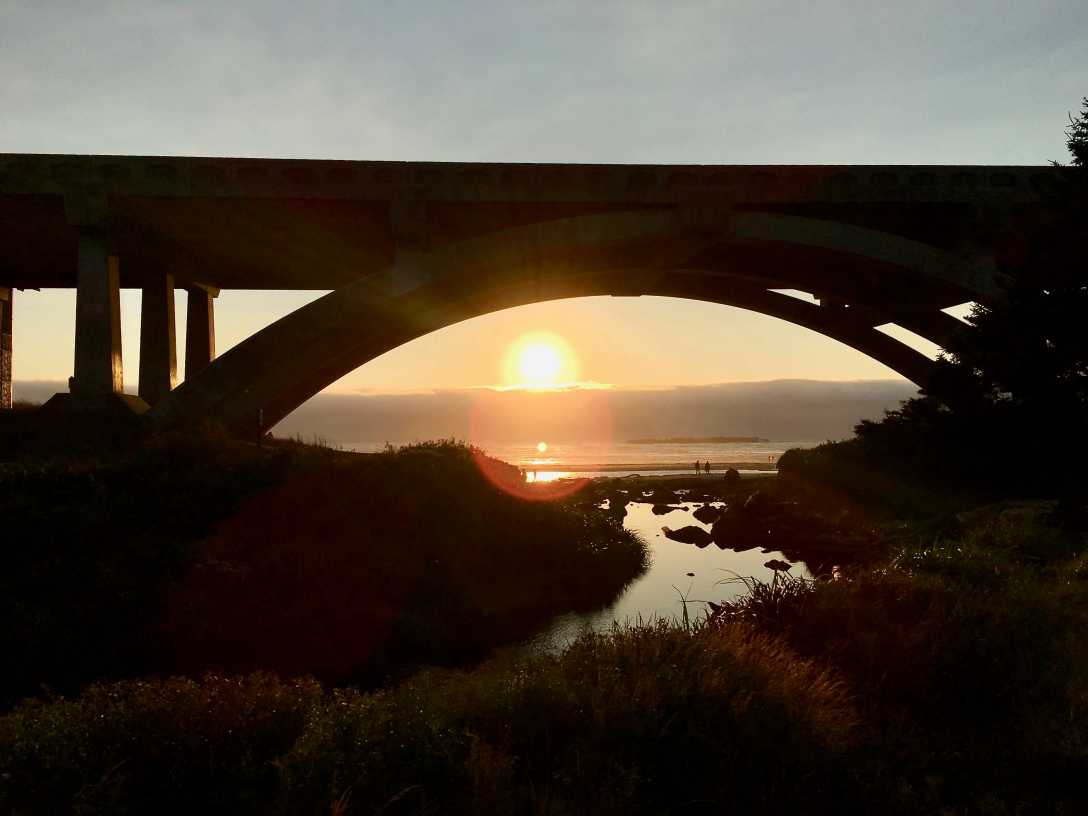 The sun sets under the Spencer Creek Bridge Beverly Beach State Park Oregon sunset